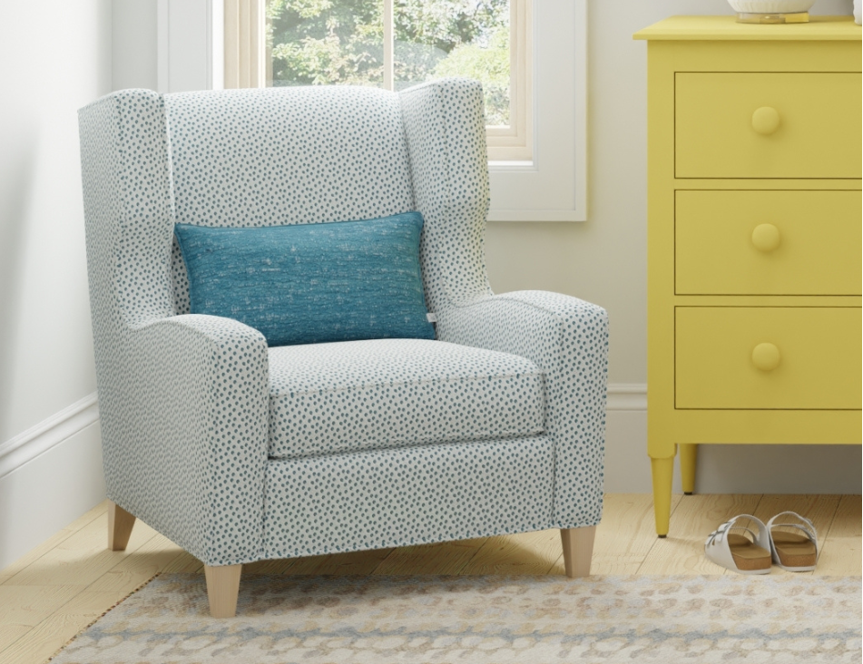 Gray armchair with a blue pillow in a room with a yellow dresser and window.